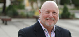 Smiling bald man in outdoor setting.